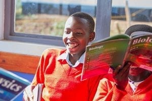 Photo of a boy from Tanzania laughing and holding a book