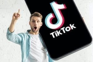 Photo of a young male holding a smartphone with TikTok app on it